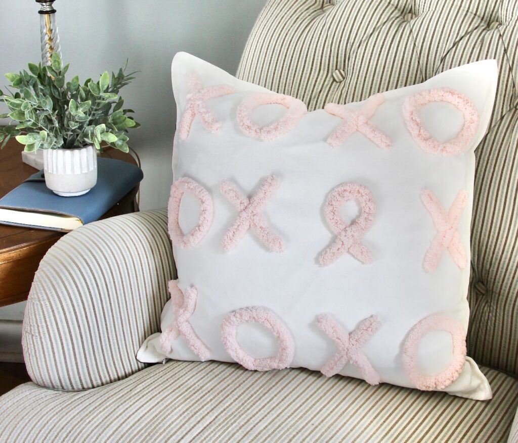 Tight picture of a throw pillow with X's and O's applied to the face except one O is shaped like a cancer ribbon