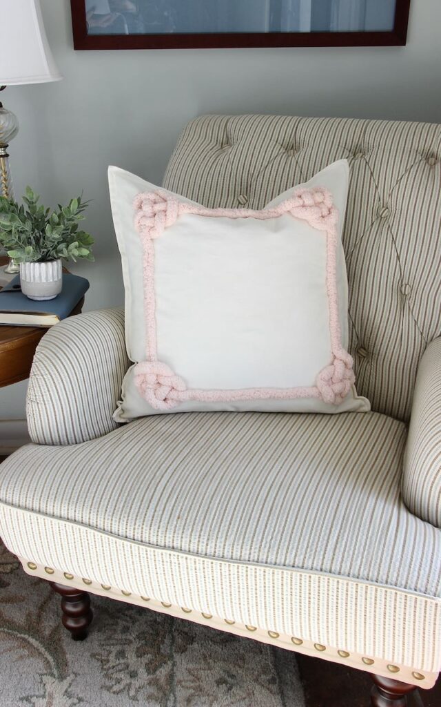 Valentines day accent pillow made with an inset frame of very thick yarn that is tied in each corner with a decorative lovers knot