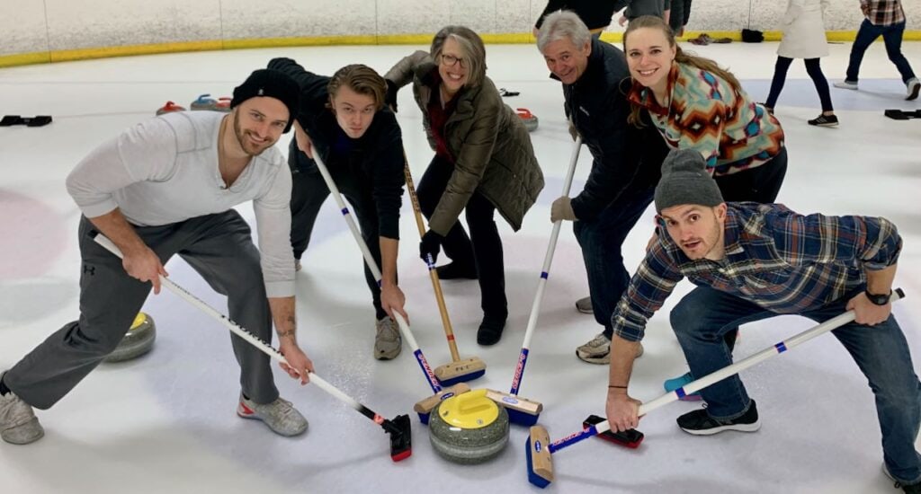 Family of six adults gathered around the curling stone as on of their activities in the family gift exchange