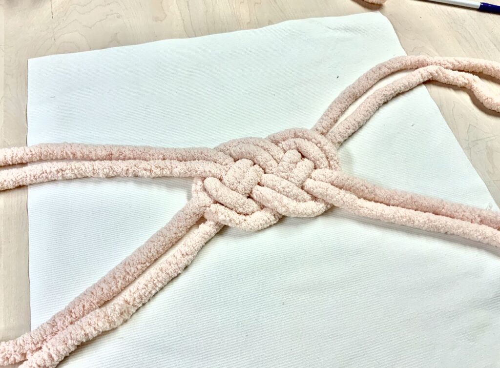 Double version of Josephine knot tied in very thick yarn laying on top of the pillow cover