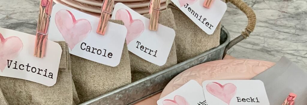 super close up of 4 washed linen party favor bags in a galvanized steel tray on a grey and white quartz countertop with a stack of pink plates ready for Galentine's Day