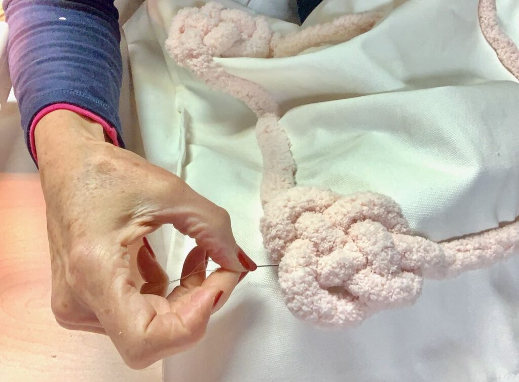 Hand pulling needle and thread through the knot on the Valentine pillow