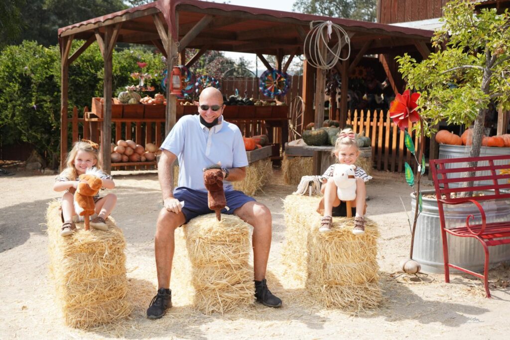 A smiling man is sitting on a hale bay horse, with a young girl on a hale bay on each side of him