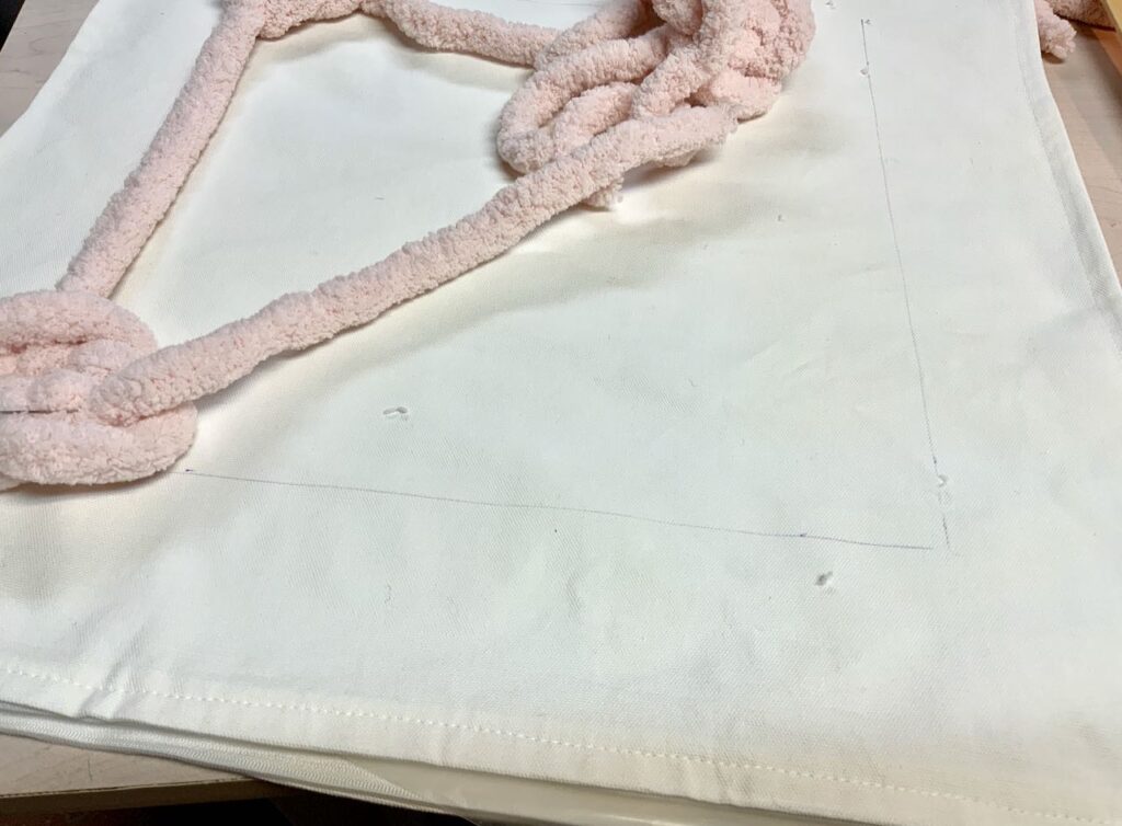Showing line for frame on the fabric with one knot in the corner and the yarn beside it