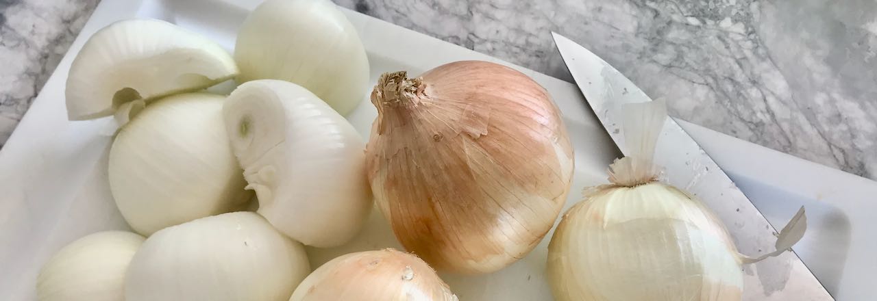 closeup of onions on a cutting board with knife on a quartz countertop