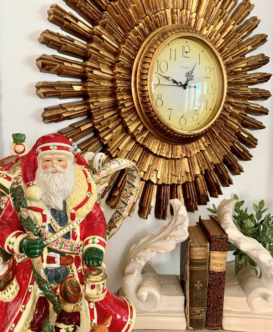 Large ceramic Santa Claus pitcher in front of a large sunburst clock and two stone bookends with two vintage books