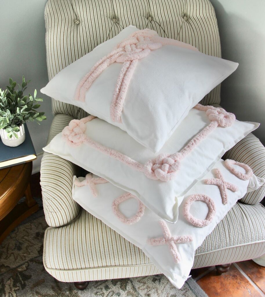 Three coordinating Valentines Day pillows are  stacked in an overstuffed chair