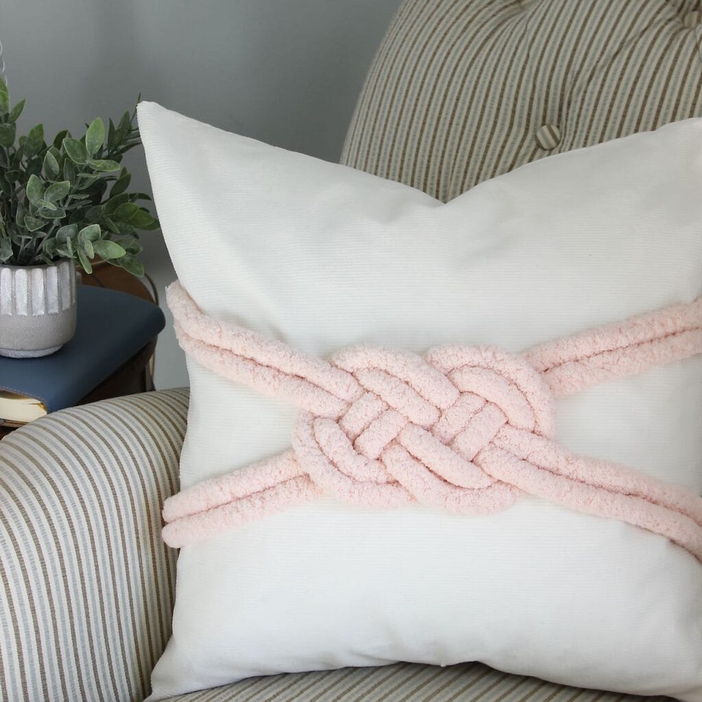 Closeup of one pillow with a heavy yarn making a large lovers knot on the front of the pillow