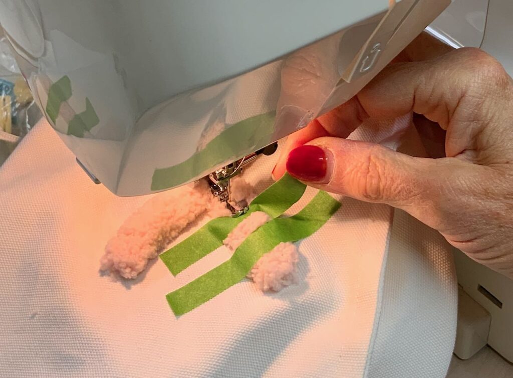 Closeup of a hand peeling back a piece of painters tape with the needle of the sewing machine in the down position