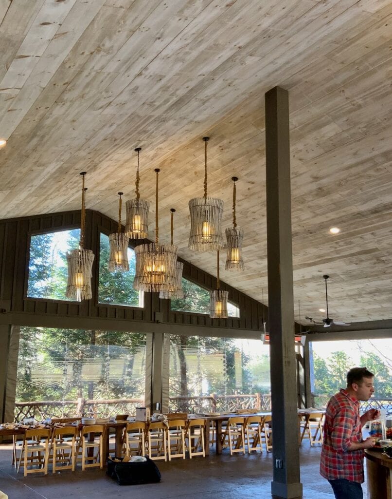 Large event venue interior with high wood beamed ceiling, gorgeous hanging basket type lights, open walls looking on the the foorested Blue Ridge mountains
