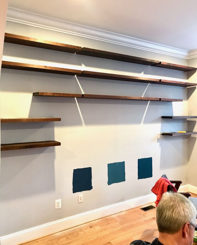 Neutral Wall the top five rows of Floating bookshelves installed. Three squares of paint samples are painted down low where the cabinets will cover it.