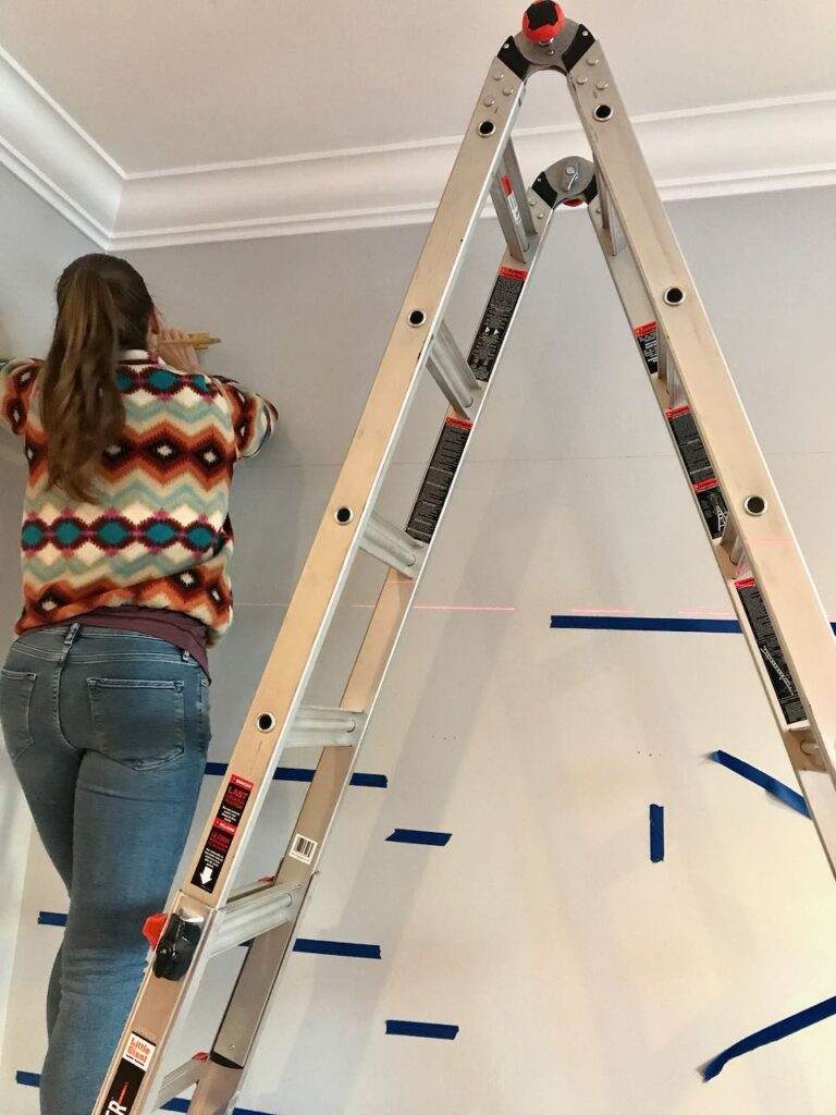back of Girl on tall ladder measuring and marking the lines for the shelves using a laser level