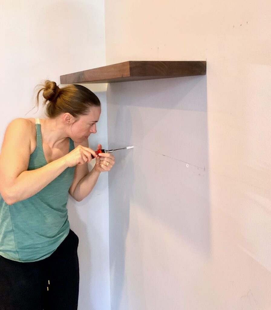 Woman with a screwdriver adding anchors in the wall for the second shelf  located just below the first one