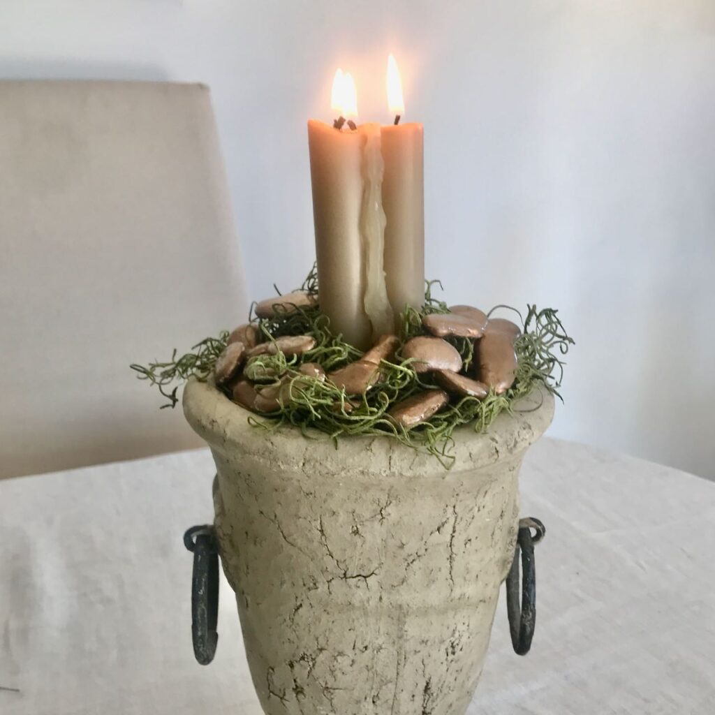 closeup of three tapers in a concrete urn surrounded by moss and bronze painted lima beans