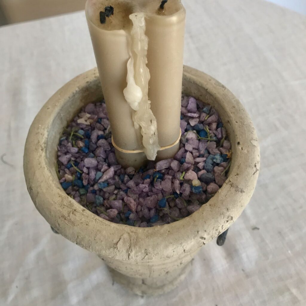 A bundle of three taper candles are held with a rubber band down low and then tucked into a concrete urn filled with aquarium gravel.