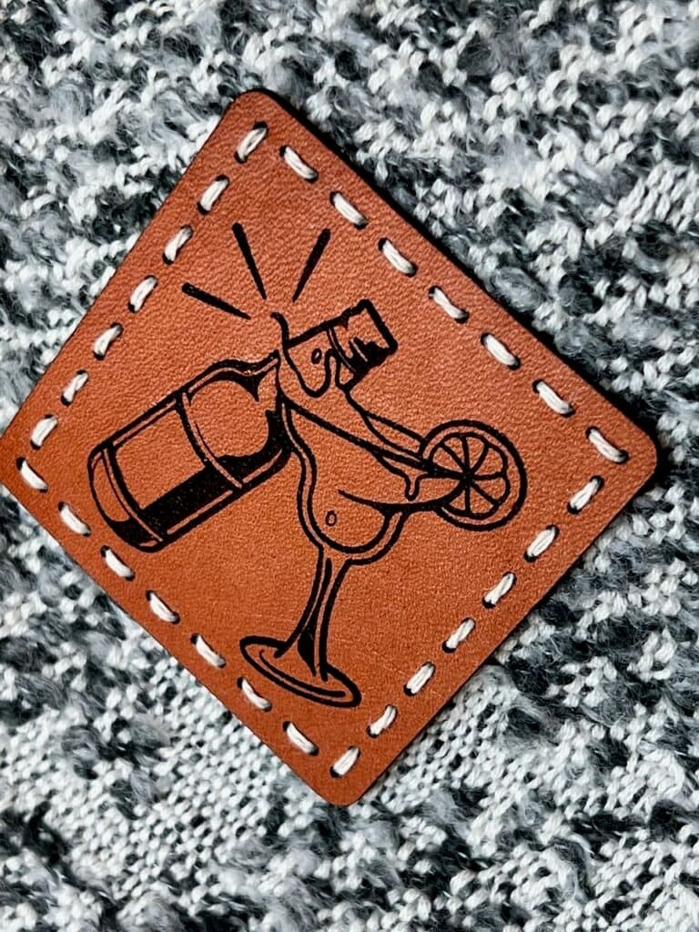 super closeup of a square leather patch embossed with a wedding logo of a beer bottle clinking with a margarita glass