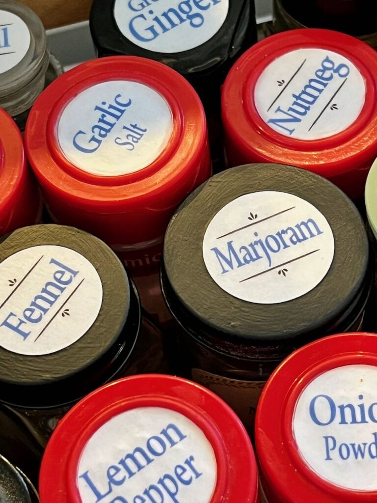 Closeup of several spice jars with labels on top of the lids and coats of decoupage finish protecting the labels