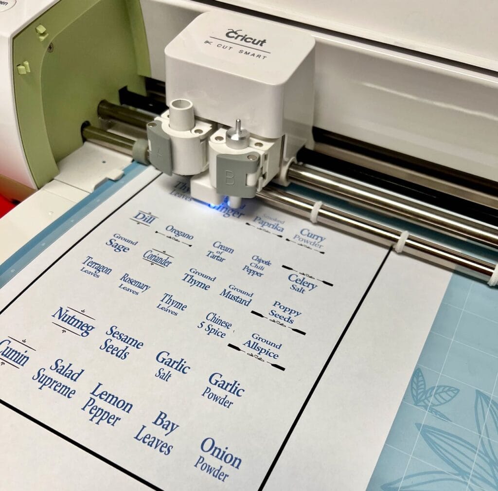 A piece of paper with labels printed on a blue backer in the cricut machine that is now cutting them into circles