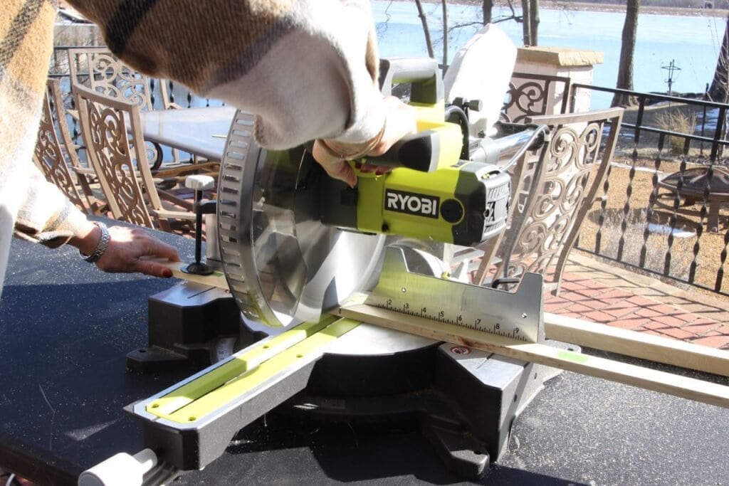 A woman's arms are using a Ryobu compound miter saw to cut furring strips to the right length