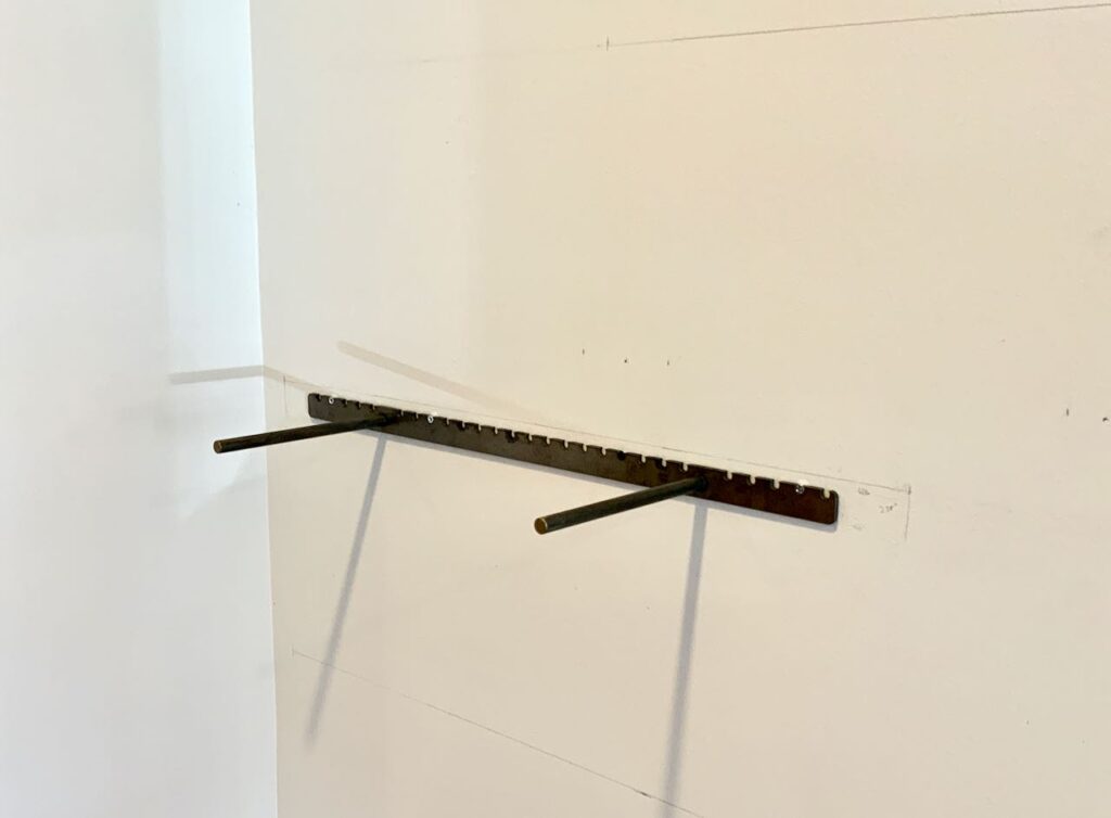 a single steel bracket for the first of the floating bookshelves is installed in a corner