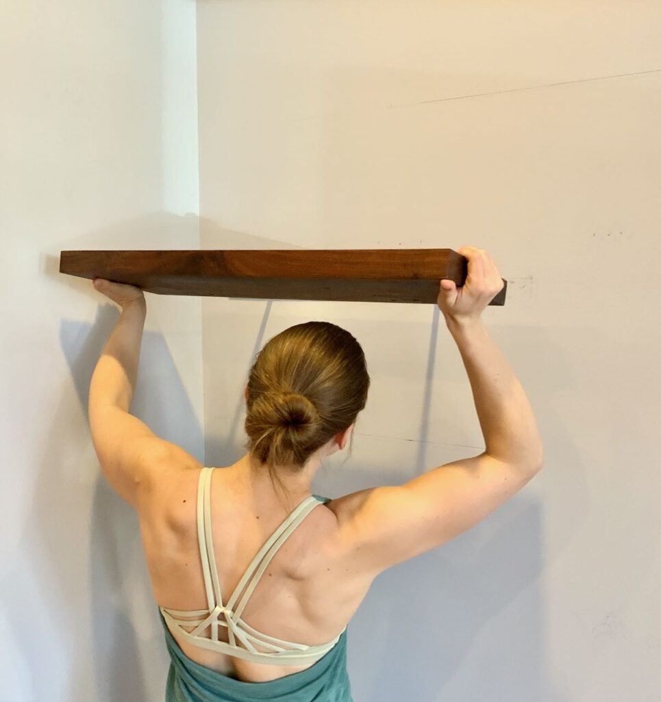 Back of a woman sliding the wood floating shelf onto the steel bracket just above her head