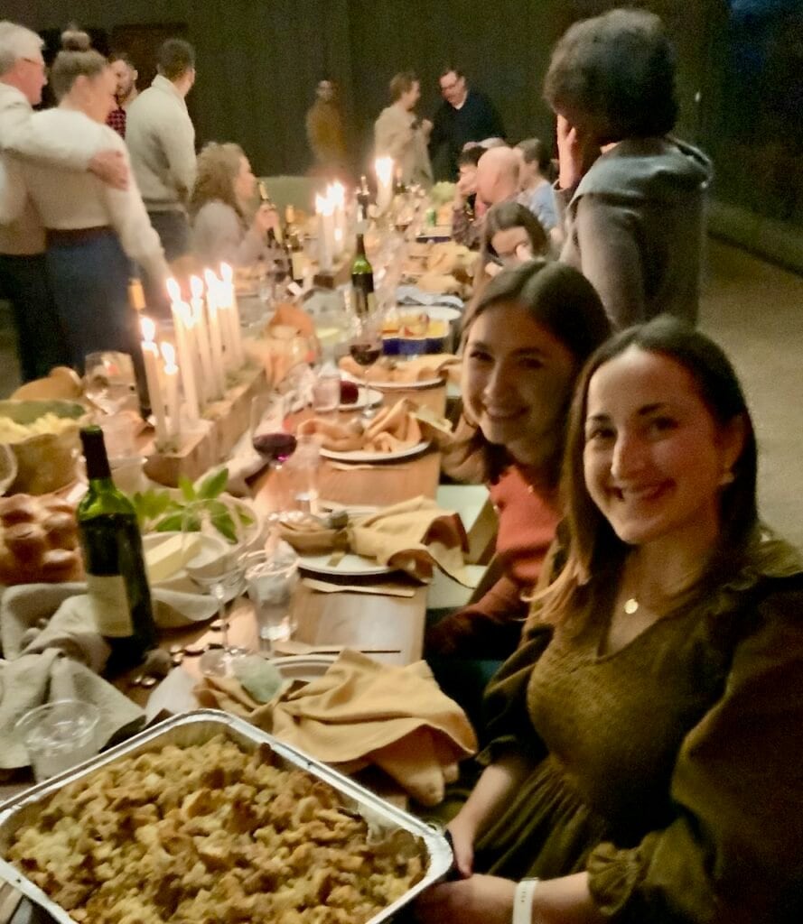 Two women in the foreground sitting at the Friendsgiving dinner table with the whole spread behind them