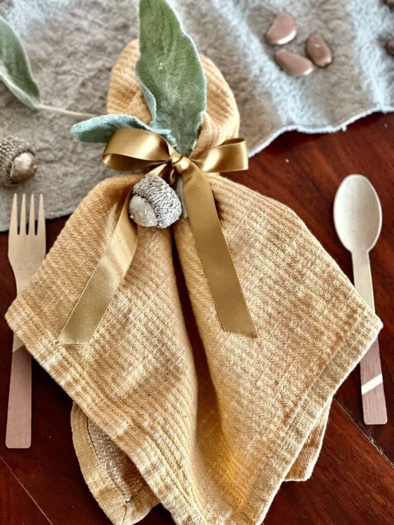 trial place setting. of gold napkin tieed with a ribbon holding two dried lambs ear leaves an acorn and embellished. bamboo fork and spoon