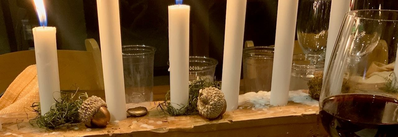 Super closeup of 7 lit candles in a block of wood candleholder with bronzed acorns