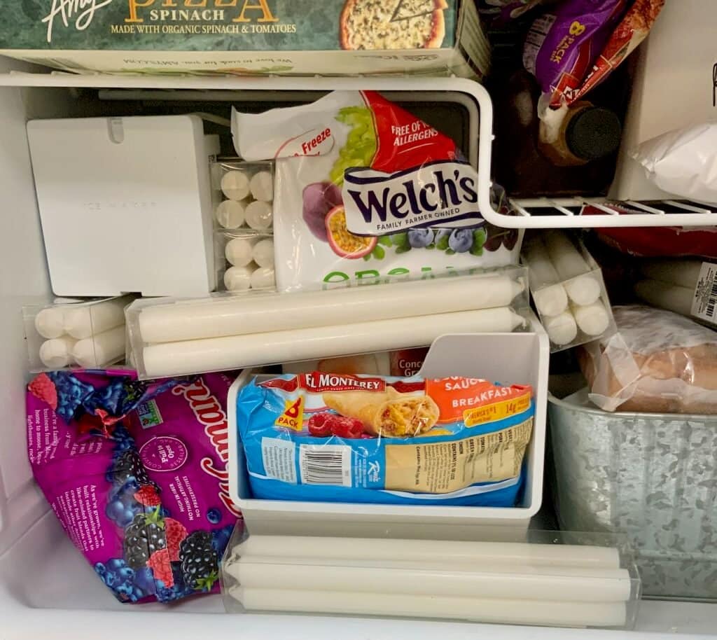 Closeup of candles between bags of frozen fruit in the freezer