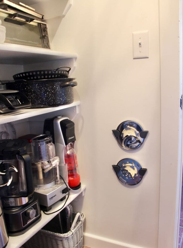 Two plastic pan lid holders installed on a white wall holding discs from a food processor