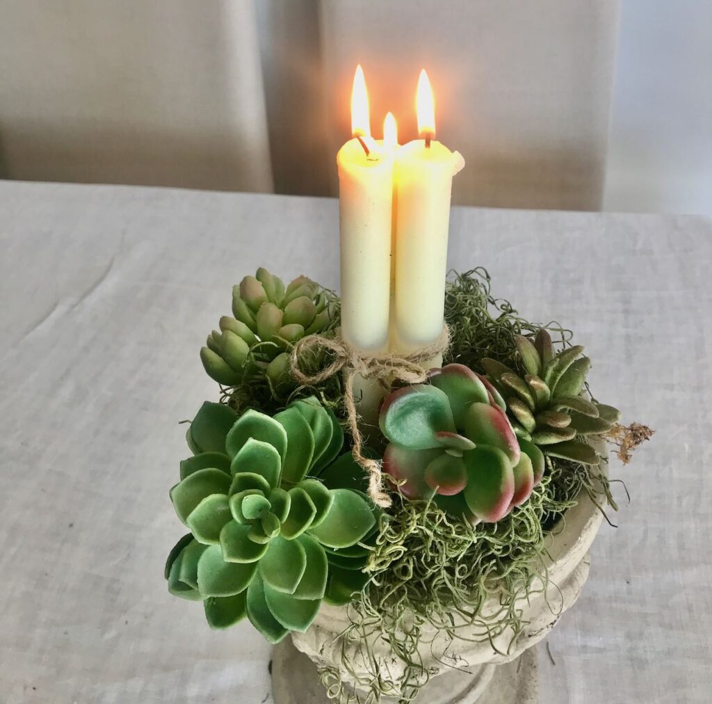 Closeup of Bundle of three tapers lit in a concrete planter surrounded with moss and a variety of succulents 