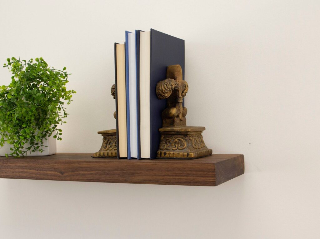 view of the end of a single walnut shelf floating on a neutral wall with a green plant and three books with bookends on it