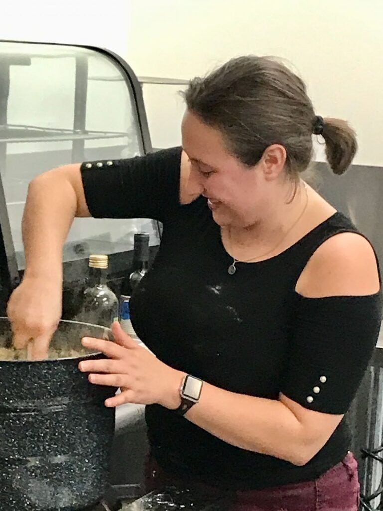 Smiling woman is stirring the ingredients of a very large pot on a commercial range