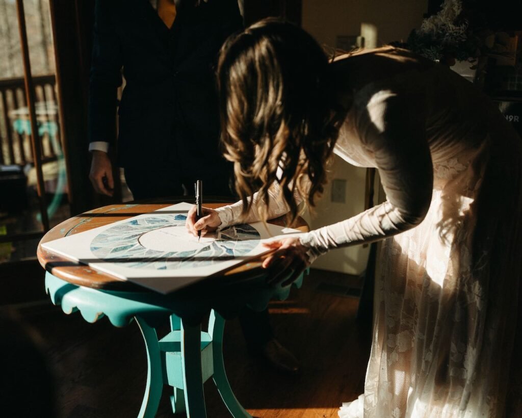 Bride is bending over a small round table signing the ketubah