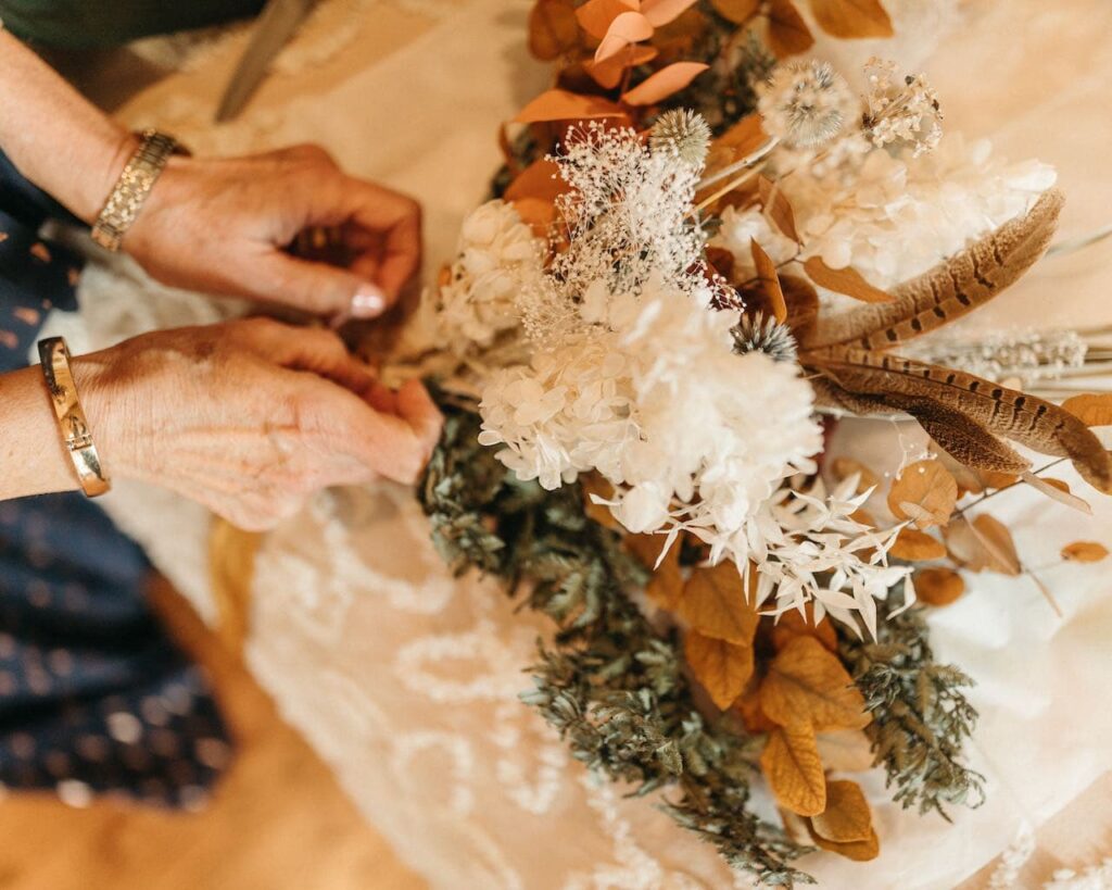 Closup of a womans hands tying long streaming ribbons around the stems of a bouquet of dried flowers