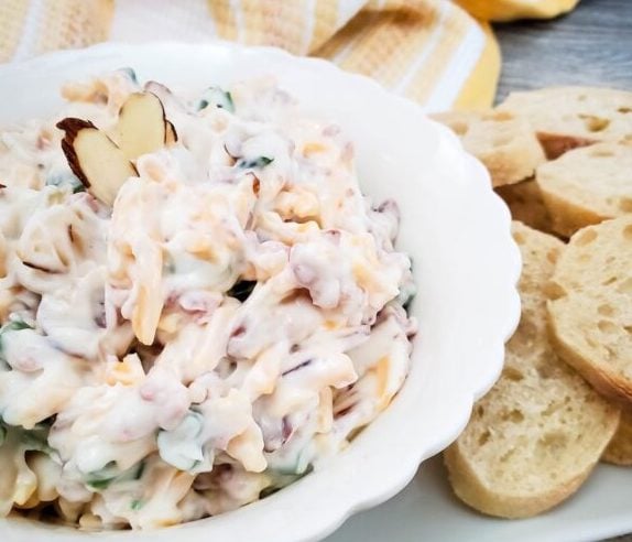 bowl of delicious looking dip with bread slices and a bright kitchen towel close by