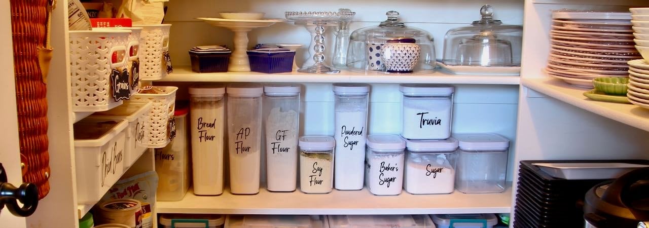 Super close up of the center section of an organized pantry with food on the left and dishes and small appliances on the right