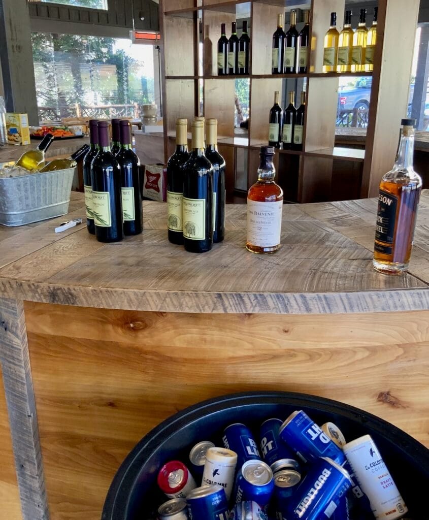 A round bar with open shelving behind is staged with bottles of wine and a tub of beer on ice