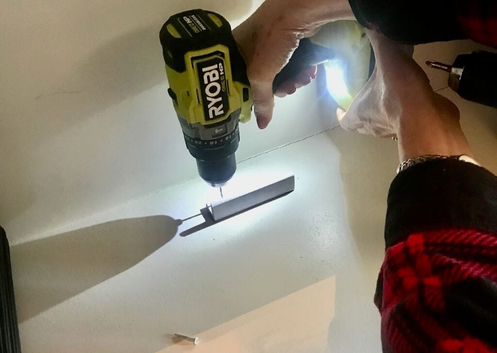 Woman's hand operating a Ryobi drill pre-drilling a hole in the L-shaped trim that will hold the platters in place