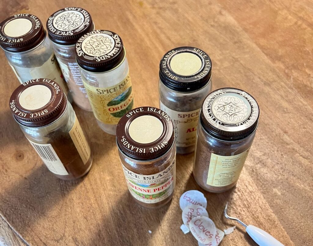 Seven Spice bottles with Spice Island lids next to a pile of old labels that I pealed off of them