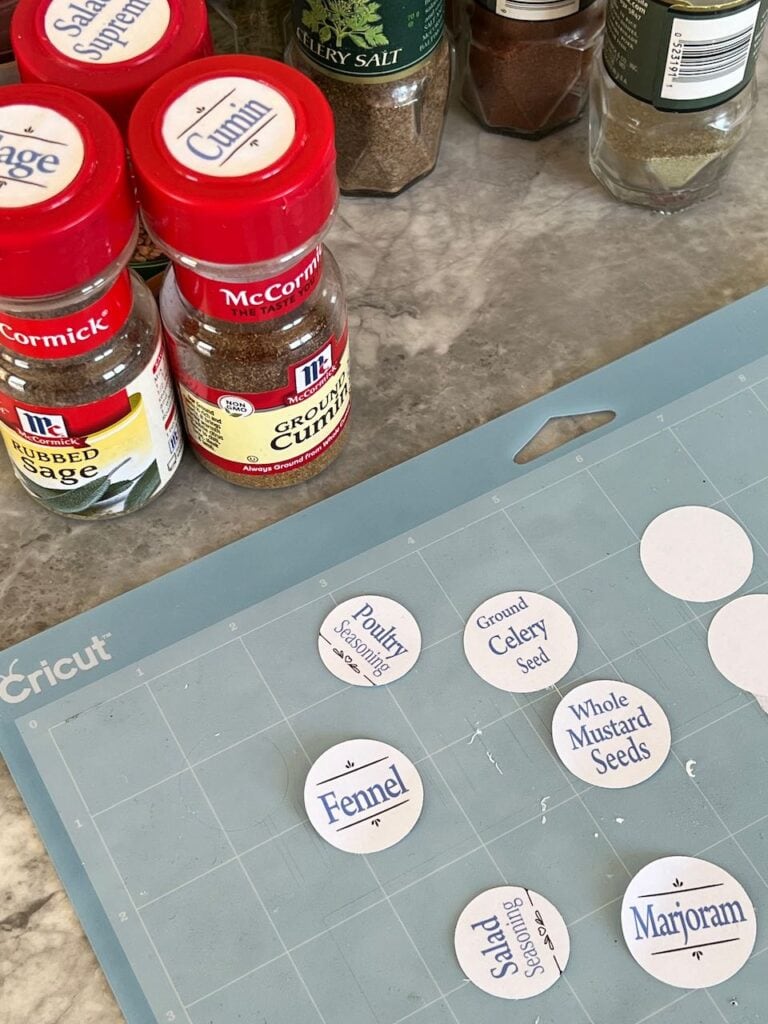 Closeup of a few spice bottle with labels next to a cricut cutting mat with a few labels on it 