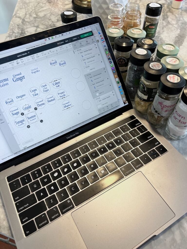 a laptop is open on quartz kitchen countertop surrounded by spice bottles and the names of the spices are drawn out on the computer screen