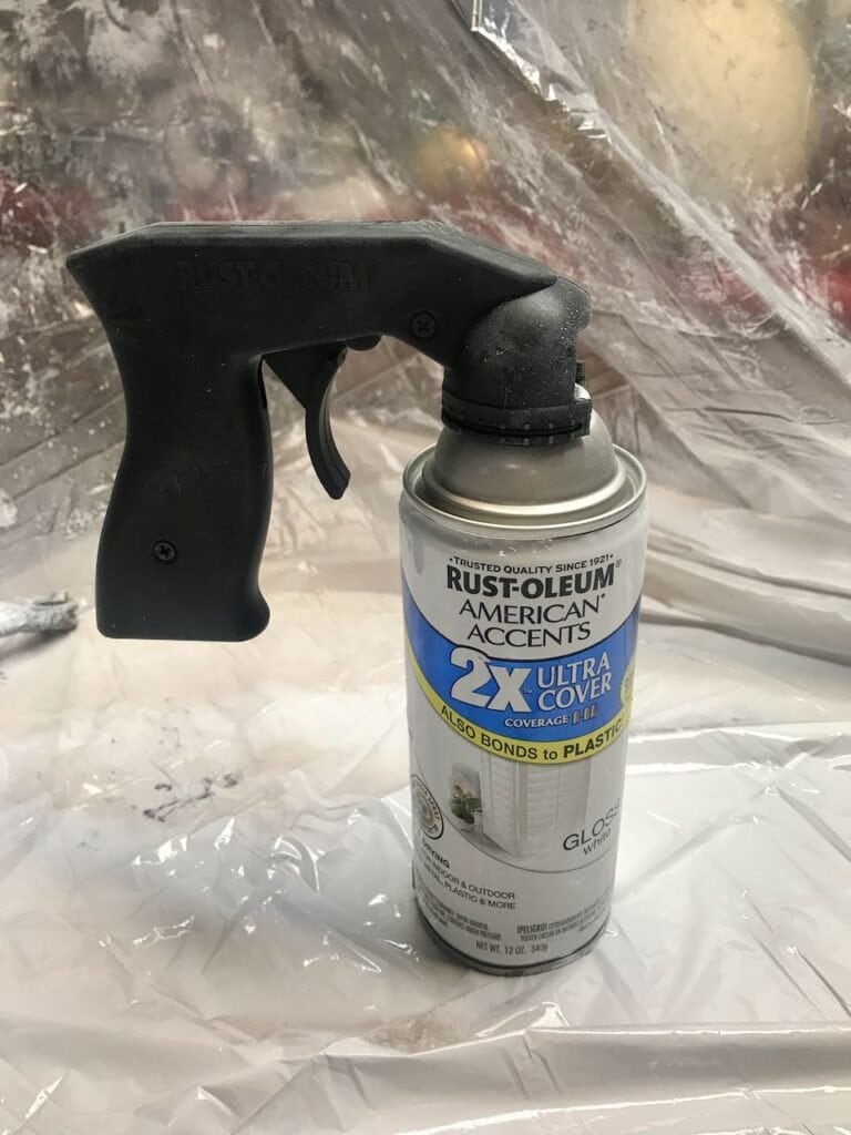 Rustoleum Spray Paint can with a pistol grip adapter attached in front of a plastic drop cloth hanging from the ceilng.