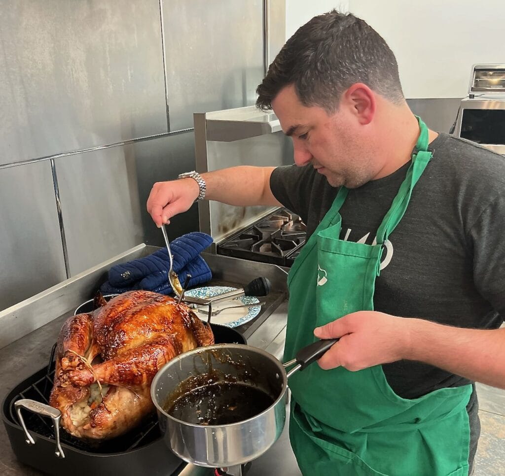 Man in apron basting a turkey on a large commercial range