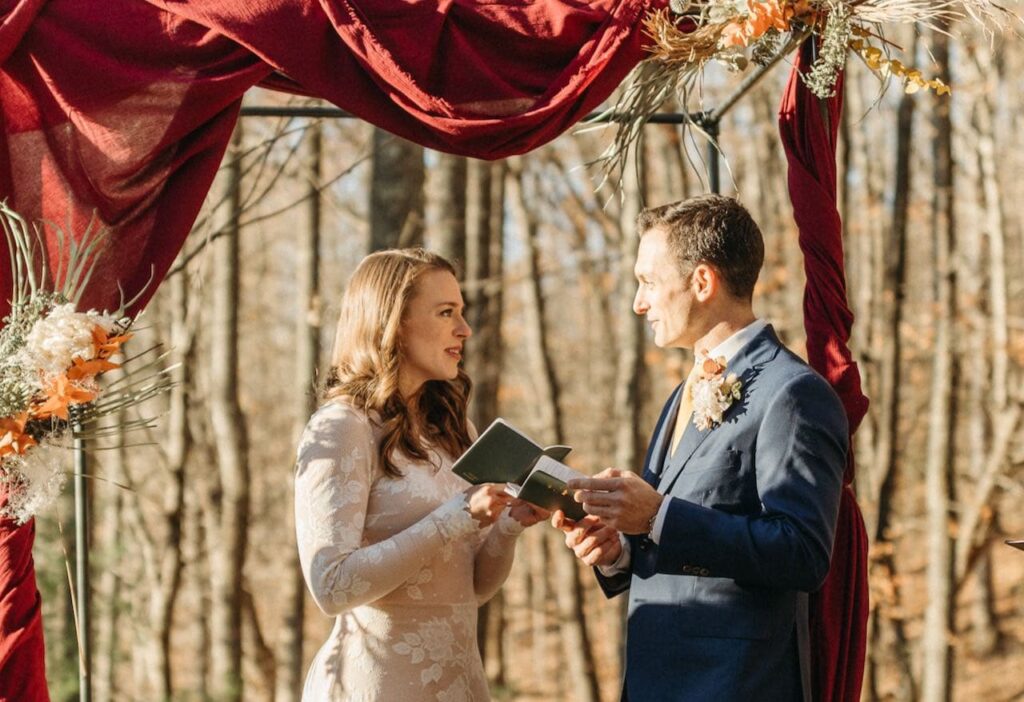 Bride and Groom facing each other outside on a mountainside holding small leather vow books as they pledge to each other