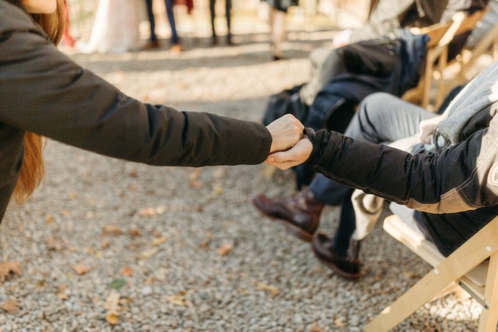 Two arms outstretched across the aisle carefully passing on the wedding bands in closed fists