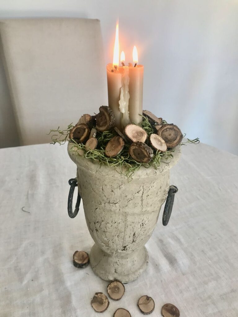 Trio of taper candles lit in a concrete urn surrounded by moss and small wood slices