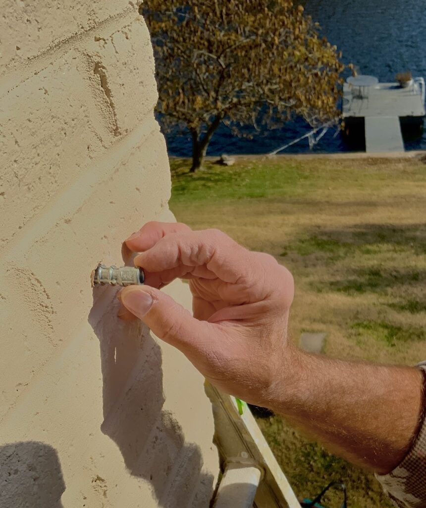 closeup of a man's hand putting an anchor into the hole drilled in the brick column