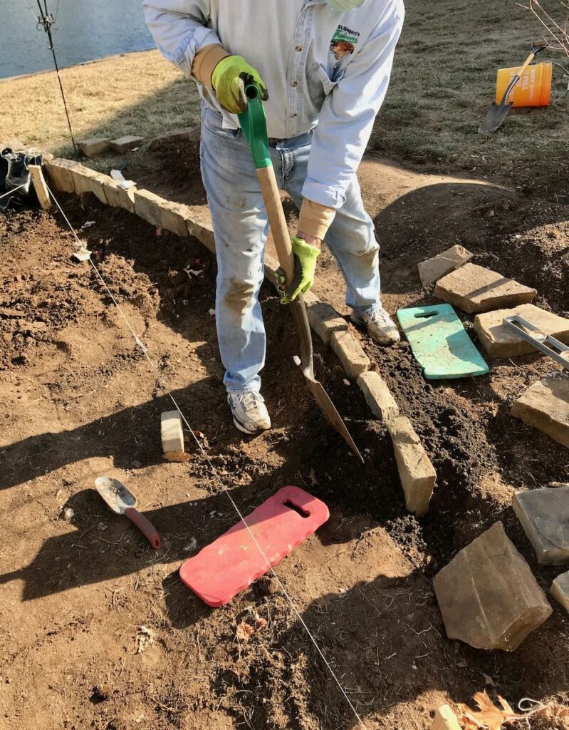 Man with a shovel backfilling beside the new stone edge to keep them in place