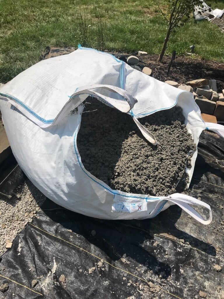 Large freight bag filled with a ton of road fill gravel delivered on the edge of the patio site.